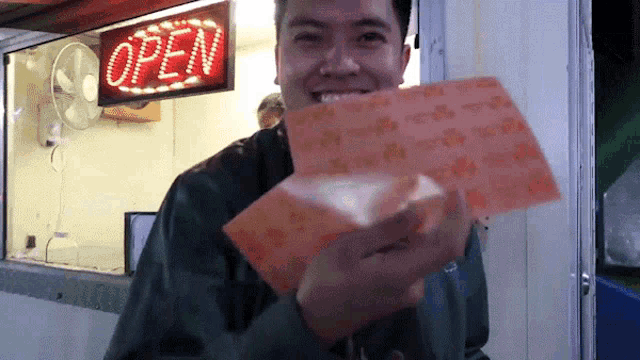 a man holding a piece of paper in front of a sign that says open