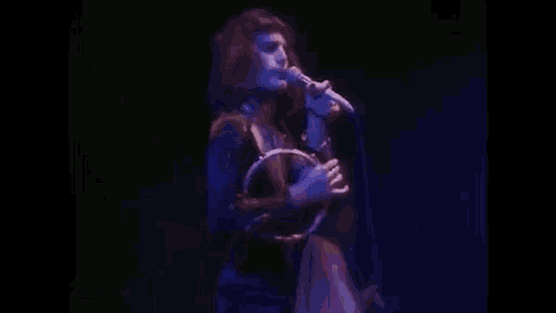 a man is singing into a microphone while playing a tambourine on stage .