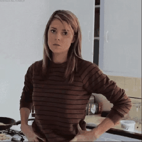 a woman is standing in a kitchen with her hands on her hips and a striped shirt on .