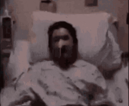 a blurry picture of a man with a beard laying in a hospital bed