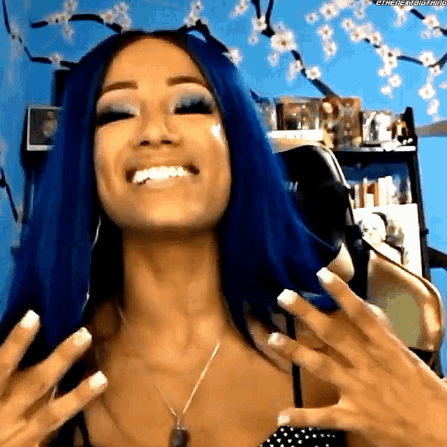 a woman with blue hair and white nails is smiling and holding her hands up