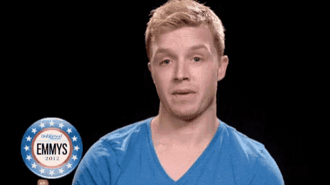 a man in a blue shirt is covering his mouth in front of a button that says emmys 2012