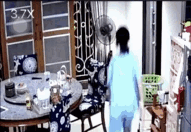 a woman in a blue shirt is standing in a room with a fan and a basket .