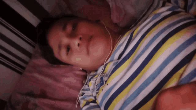 a person wearing headphones and a striped shirt is laying in bed