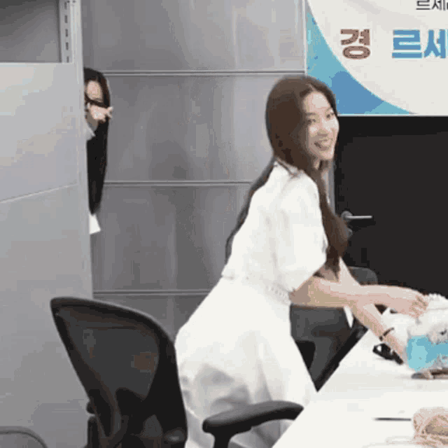 a woman in a white dress is sitting at a desk in front of a sign that says ' a ' on it