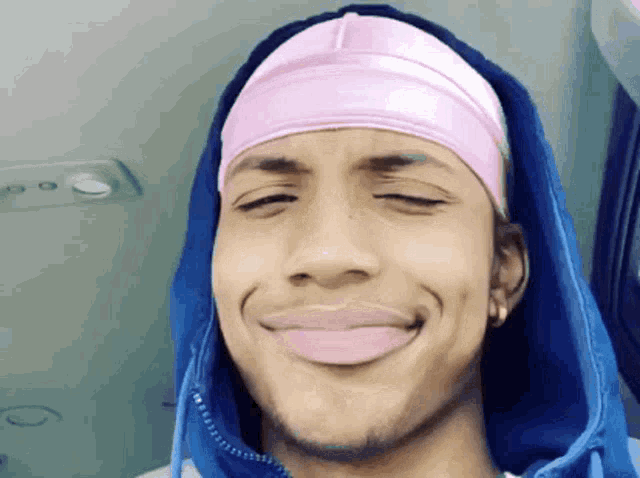a man wearing a blue hoodie and a pink headband smiles for the camera