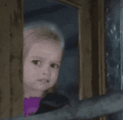a little girl is looking out of a window with a sad look on her face .