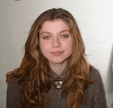 a woman with long red hair is wearing a grey shirt and a heart necklace