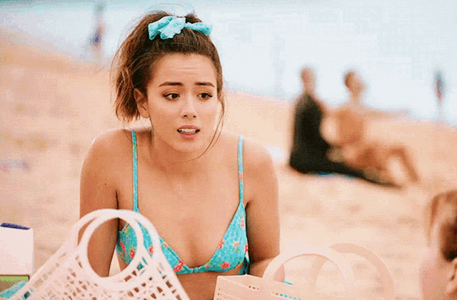 a woman in a bikini is sitting on the beach holding a pink bag