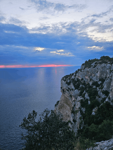 a cliff overlooking a body of water with a cloudy sky