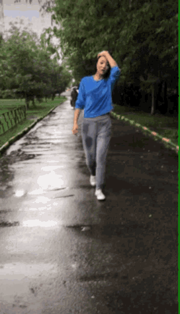 a woman in a blue shirt and sweatpants is walking down a wet street