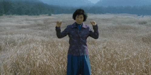 a woman in a purple jacket stands in a field of tall grass with the word wan written on the bottom