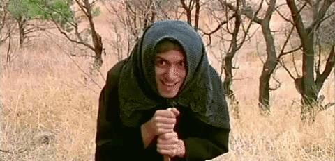 a man wearing a scarf around his head is standing in a field holding a stick .