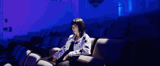 a woman sits in an auditorium with purple lights