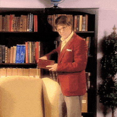 a man in a red jacket is standing in front of a bookshelf holding a book that says ' i love you '