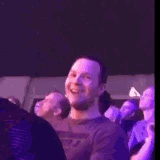 a man in a purple shirt is smiling while sitting in a crowd of people .