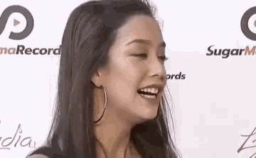 a woman wearing hoop earrings is smiling with her eyes closed in front of a white wall .