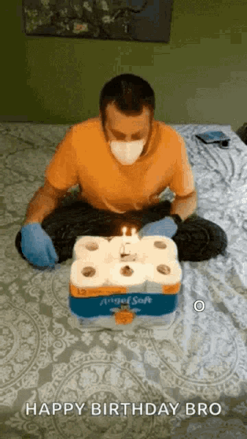 a man wearing a mask and gloves is sitting on a bed with a birthday cake made out of toilet paper rolls
