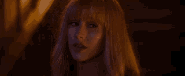 a close up of a woman 's face with long blonde hair and bangs in a dark room .