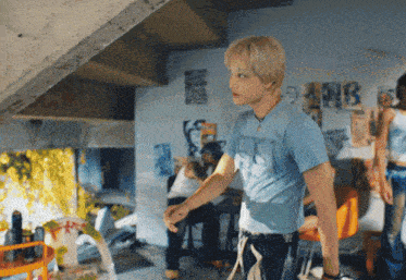 a man in a blue t-shirt stands in a room with graffiti on the walls including one that says mb