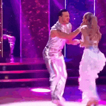 a man and a woman are dancing on a stage . the woman is wearing a white dress .