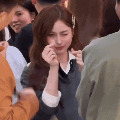a woman making a heart shape with her hands in a crowd of people