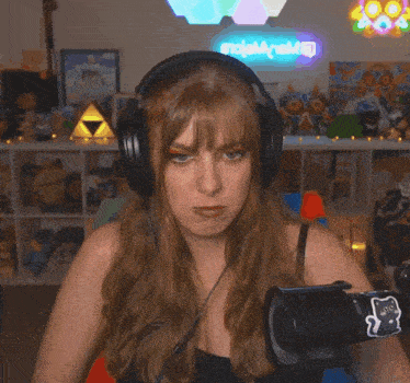 a woman wearing headphones looks at the camera in front of a neon sign that says " zelda world " on it