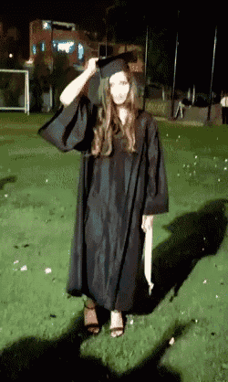 a woman in a graduation cap and gown stands in a field at night