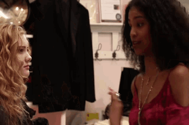 two women are standing next to each other in a room talking .