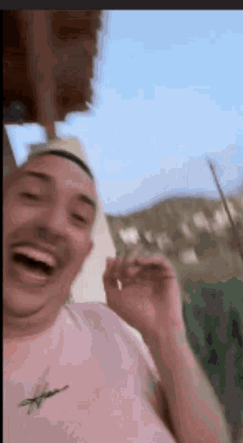a man wearing a hat and a pink shirt is laughing while holding a cigarette .