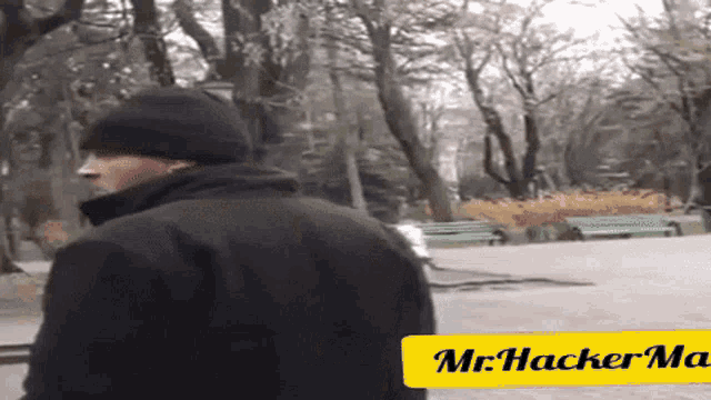 a man standing in a park with a yellow sign that says mr hacker ma