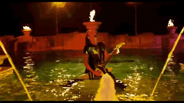 a man playing a guitar in a pool with a fountain behind him