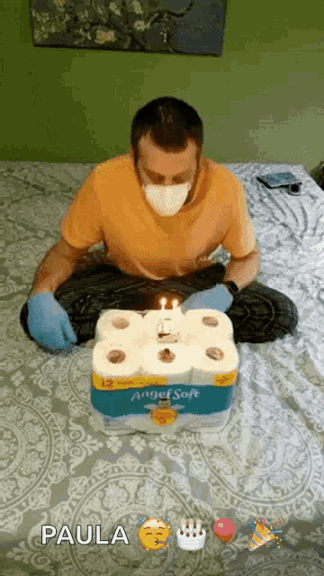 a man wearing a mask and gloves is sitting on a bed with a birthday cake made out of toilet paper rolls