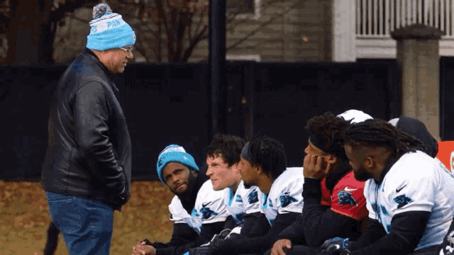 a man wearing a blue panthers hat talks to a group of players