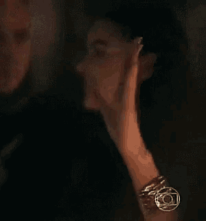 a man and a woman are standing next to each other in a dark room . the woman is holding her hand to her face .