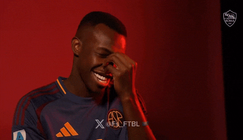 a young man wearing a purple and orange adidas shirt smiles in front of a red background