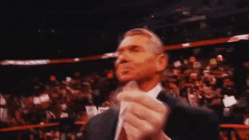 a man in a suit and tie is standing in front of a crowd in a stadium holding something in his hand .