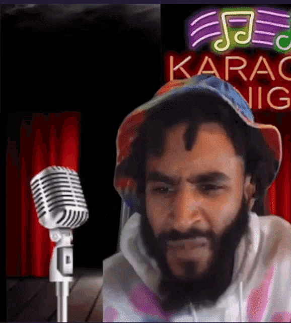 a man with a beard is standing in front of a microphone in front of a sign that says karao nig