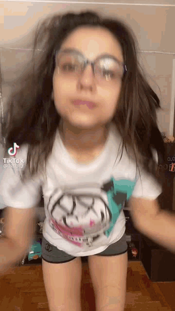 a girl wearing glasses and shorts is dancing in a room .