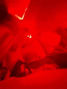 a person is laying on a bed in a dark room with a red light shining on them .