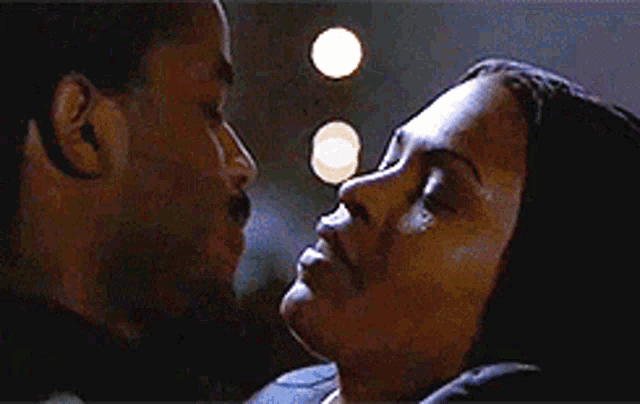 a man and a woman are kissing in a dark room with lights in the background .