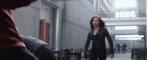 a woman in a black jacket is walking down a hallway .