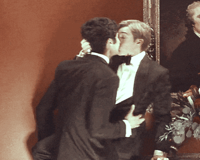 a man in a tuxedo kisses another man in front of a painting