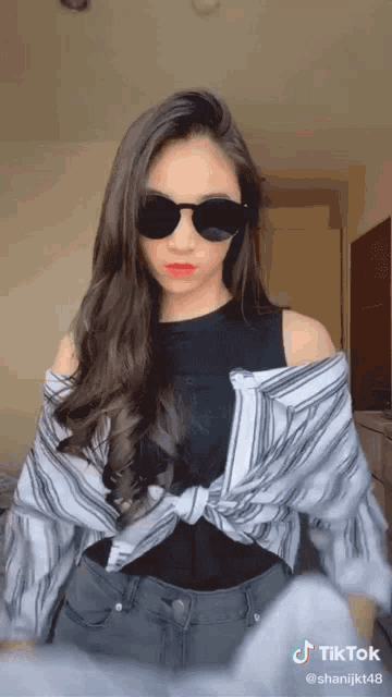 a woman wearing sunglasses and a striped shirt has a tiktok account behind her