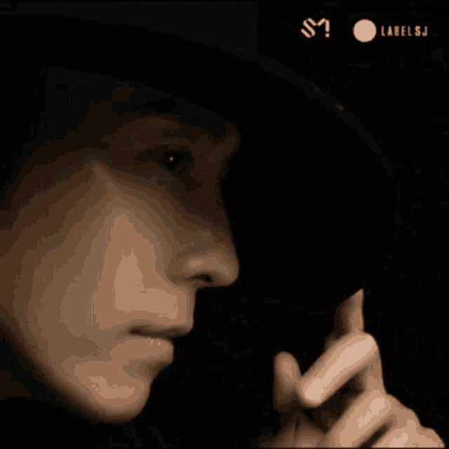 a close up of a person wearing a hat and covering their face with their hand .