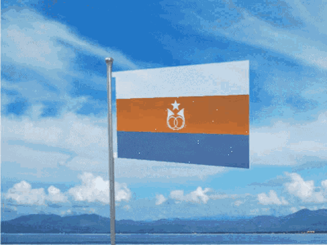an orange white and blue flag is waving in the wind with mountains in the background