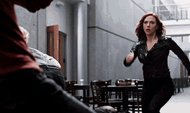 a woman in a black leather jacket is running in a hallway