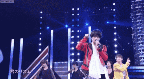 a young man in a red jacket is singing into a microphone .