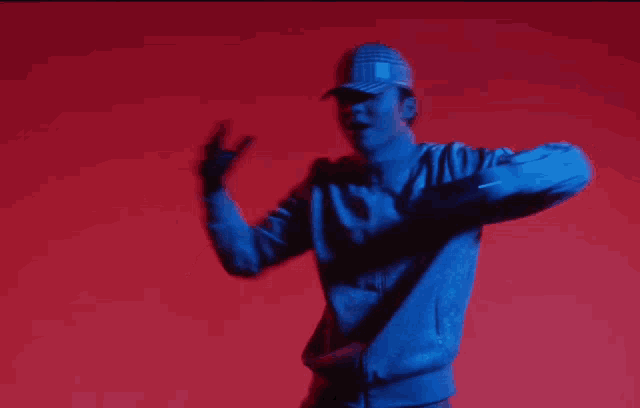 a man wearing a blue jacket and a plaid hat is dancing in front of a red background