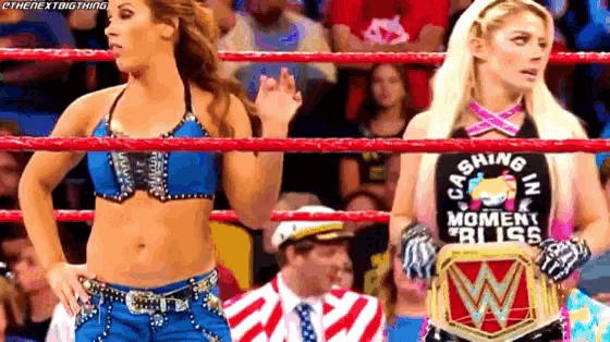 two women are standing in a wrestling ring and one of them is holding a wrestling championship belt .
